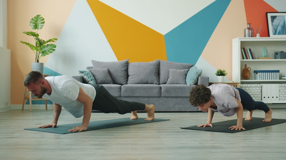 Male and female yoga students are practising downward dog position at home focused on practice on mats, people are moving simultaneously doing asanas.